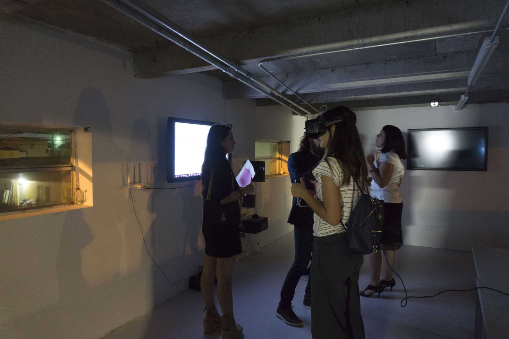 People in a room using VR headsets and looking at the screens on the walls, at the Media Under Dystopia 1.0 event